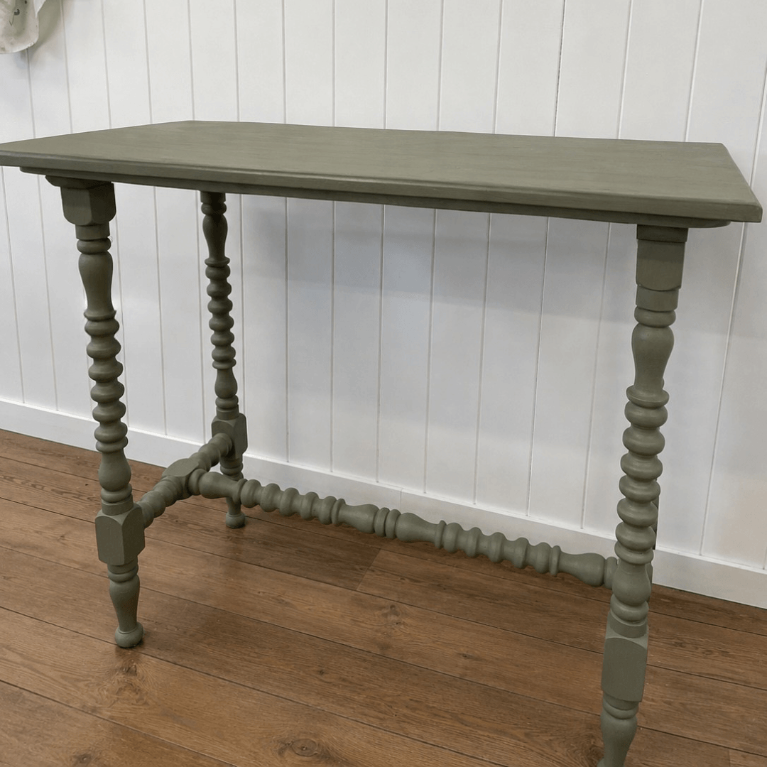 Green wooden table with spindle legs against a white paneled wall.