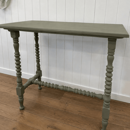 Green wooden table with spindle legs against a white paneled wall.