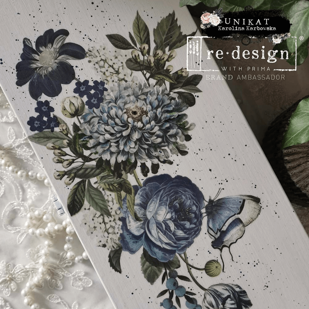 Floral design with blue flowers and a butterfly on a white background, featuring the brand 're-design with Prima'.