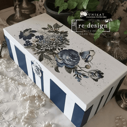 Decorative box with floral design and blue stripes on a lace surface, featuring 're-design' branding.