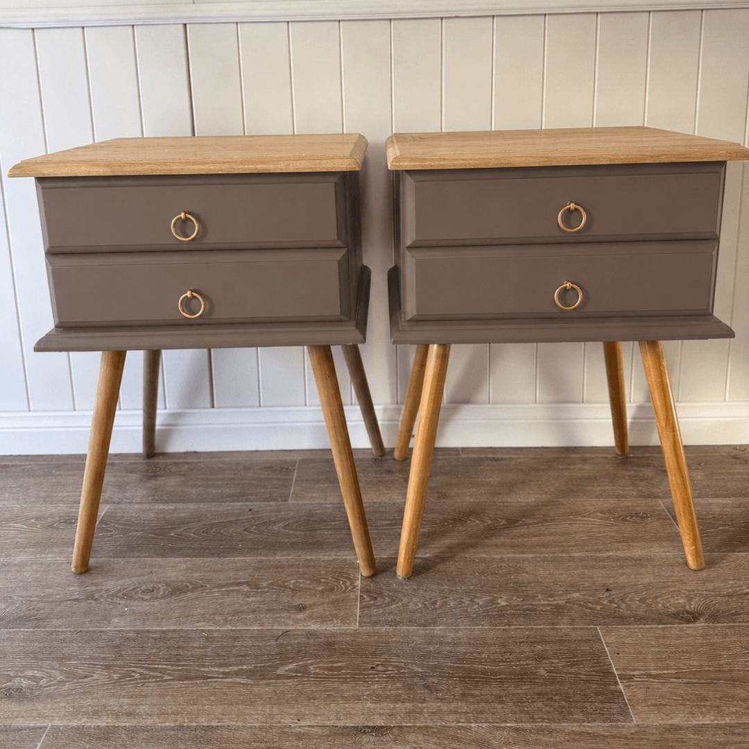 Two wooden nightstands with a grayish-brown finish and gold ring handles against a white paneled wall.