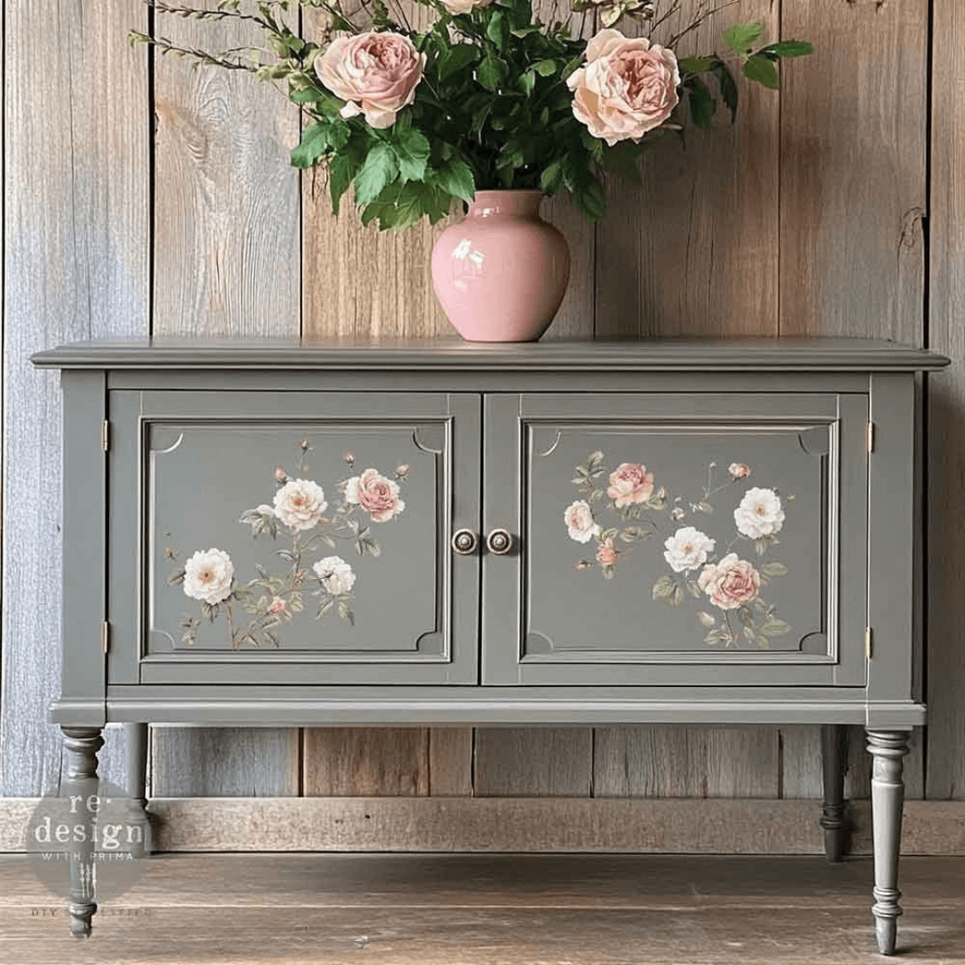 Gray cabinet with floral designs on doors, pink vase with flowers on top against a wooden wall.