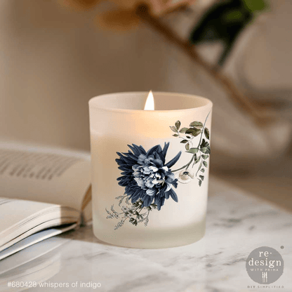 Frosted candle with floral design on a marble surface next to an open book.