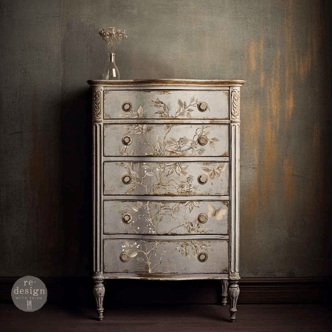 A distressed vintage-style five-drawer chest of drawers with floral hand-painted detailing, set against a textured dark gray wall.